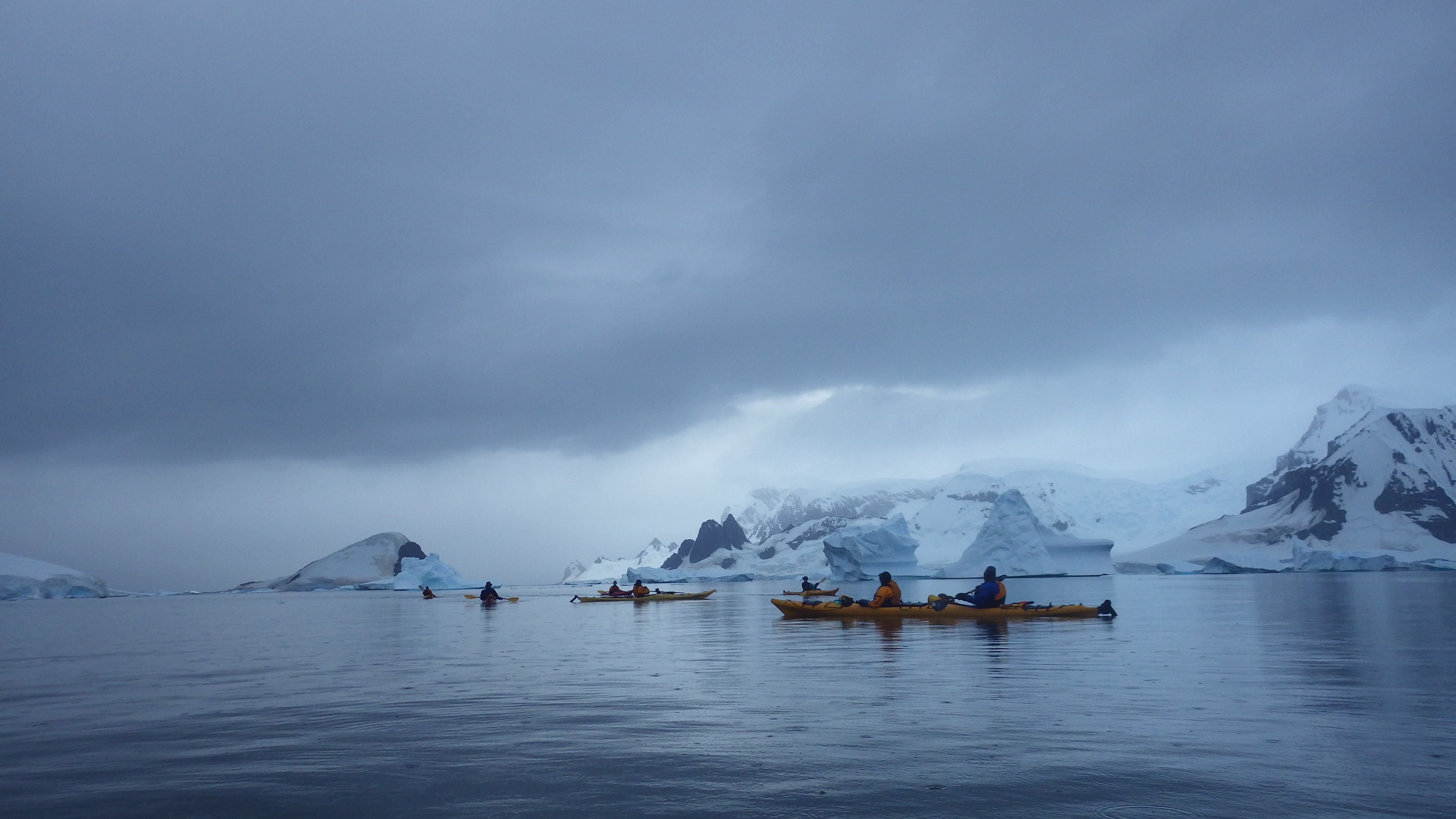 Two sea kayaks on expedition in Antarctica, icebergs behind.